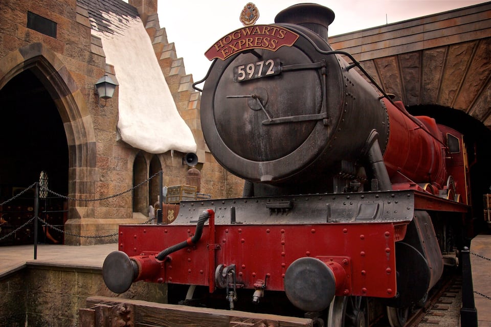 Une locomotive à vapeur portant le numéro 5972, et portant l’inscription « Poudlard Express », était garée dans une gare dotée d’arcades en pierre et d’une barrière à chaînes.