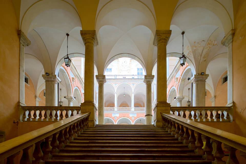 A grand staircase with a balustrade, leading to an arched balcony with a red-tiled floor.