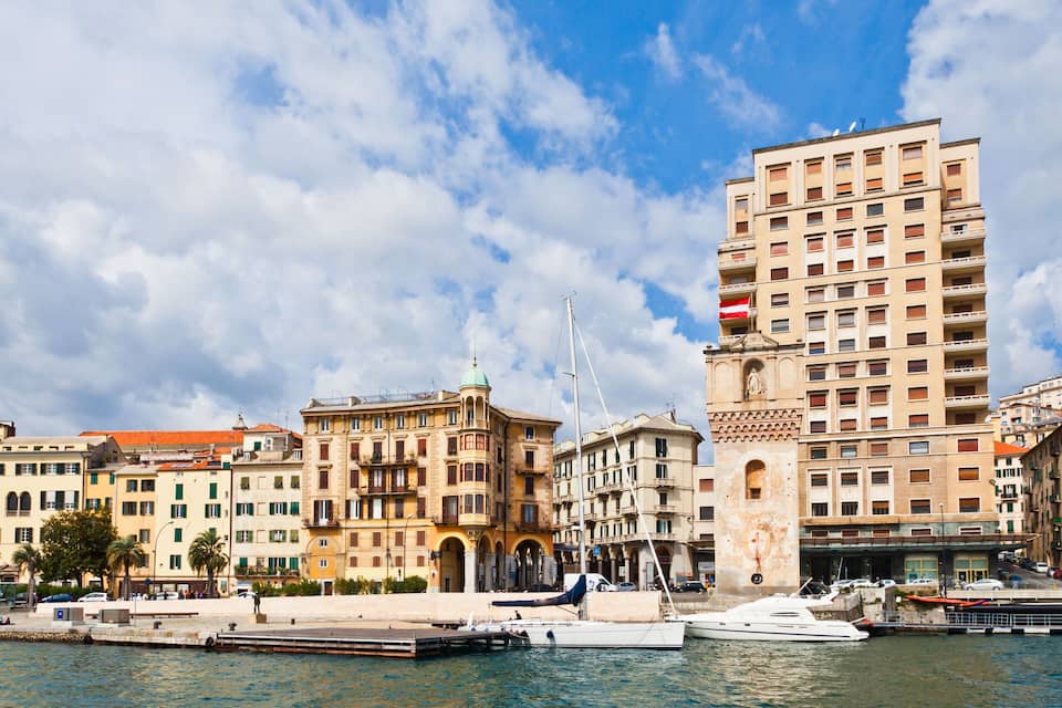 Uma orla com edifícios históricos, uma estátua e uma marina com barcos.