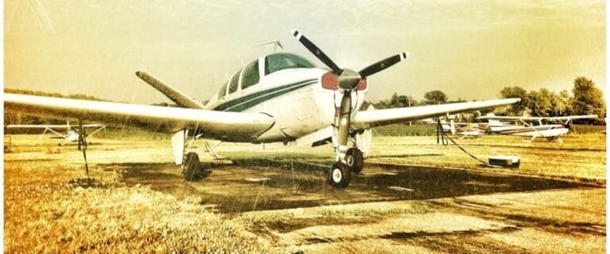 A small airplane on a grassy field, another airplane with a red and white tail, and a third airplane parked on a runway.