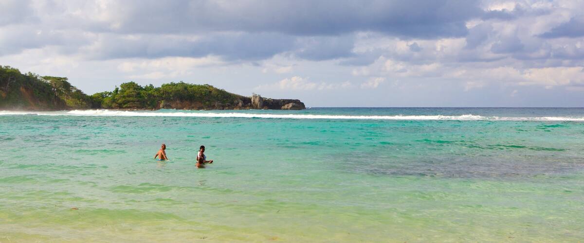 A beach with clear turquoise water, a rocky coastline, and a small structure on a cliff.