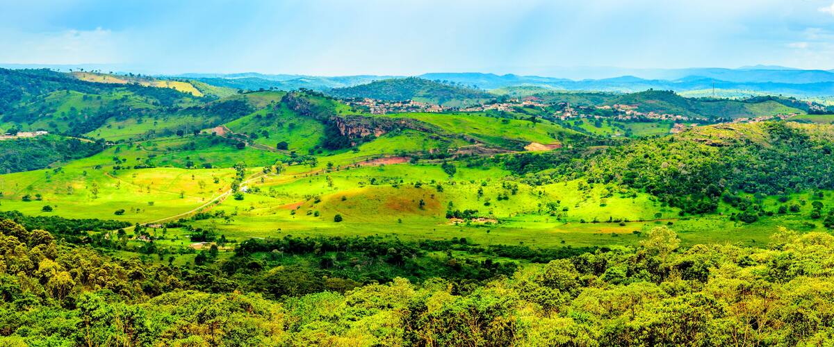 A lush green valley with rolling hills, scattered houses, and dense forested areas.