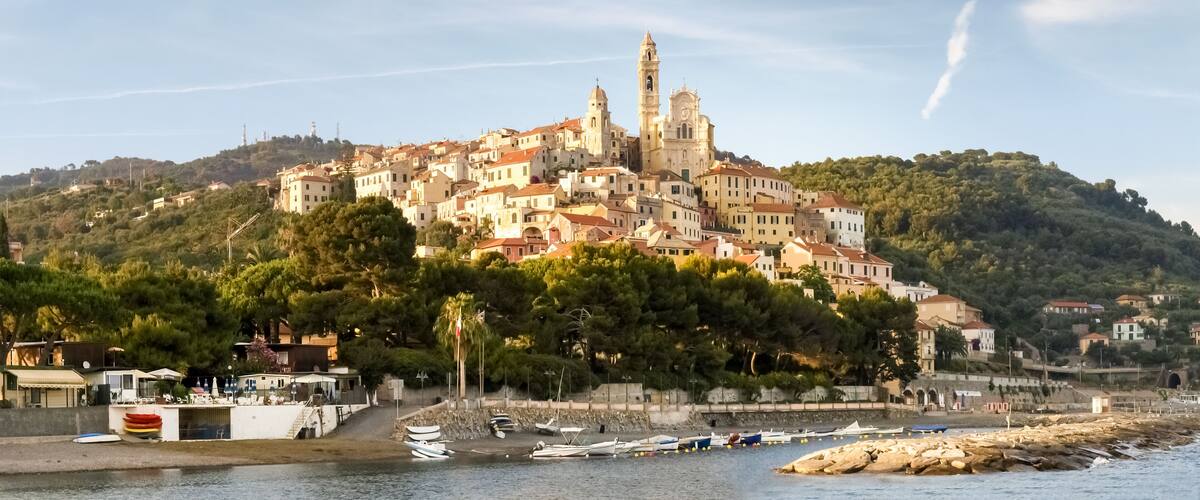 A coastal town with a prominent church on a hill, boats docked along the shore, and lush greenery.