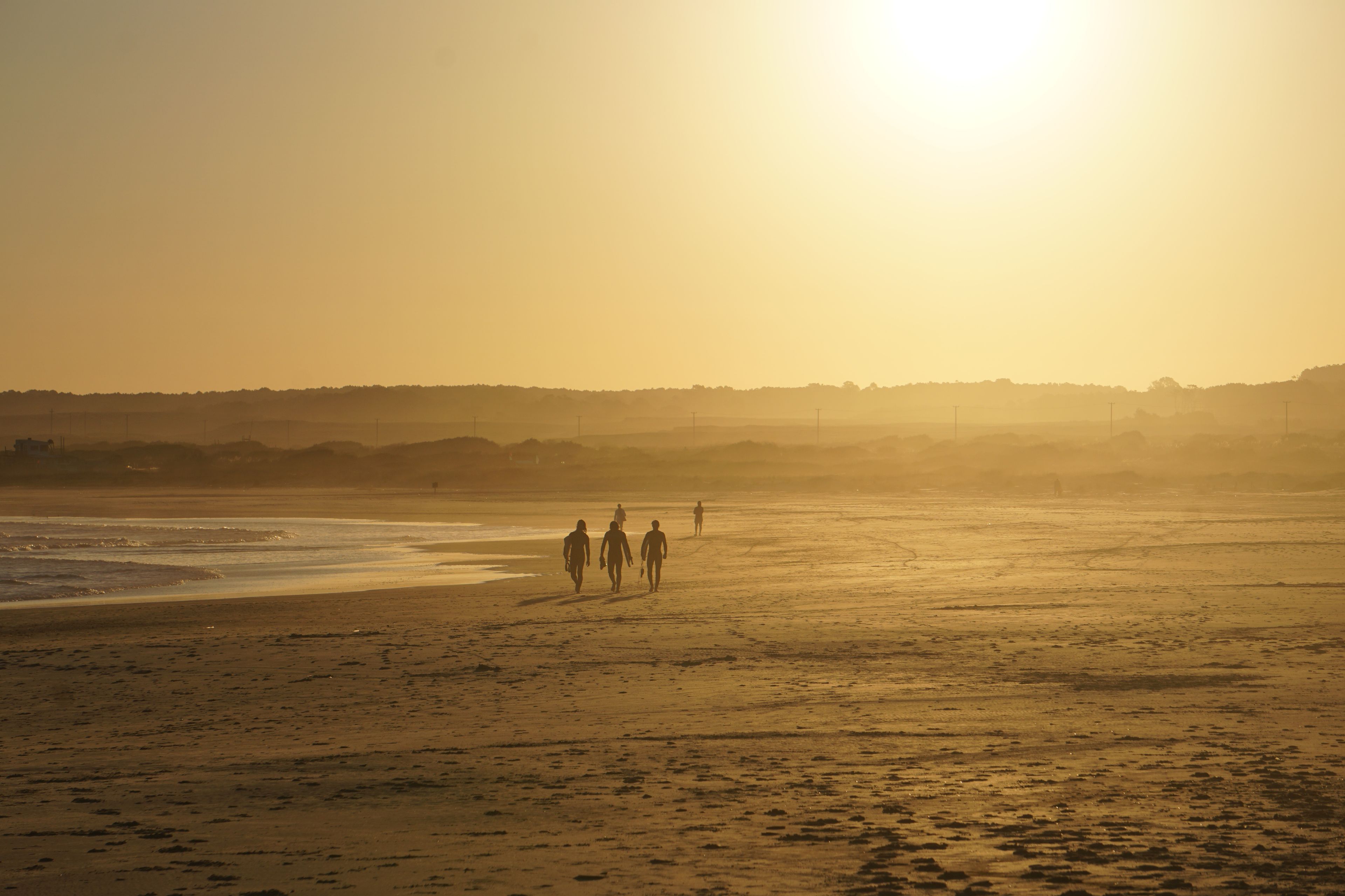 Une plage où l’on voit des empreintes de pas menant à l’eau, un coucher de soleil en arrière-plan et un horizon brumeux.