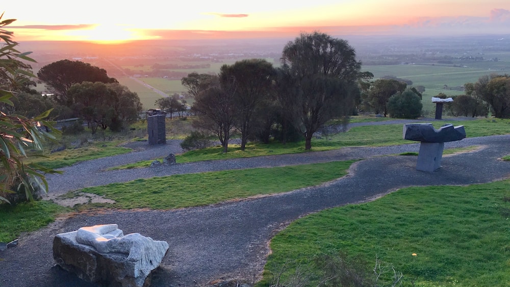 Un paysage rural avec un sentier sinueux, des constructions en pierre et un coucher de soleil en arrière-plan.