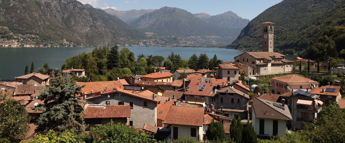 A mountainous village with terracotta-roofed buildings, a church with a bell tower, and a lake in the background.