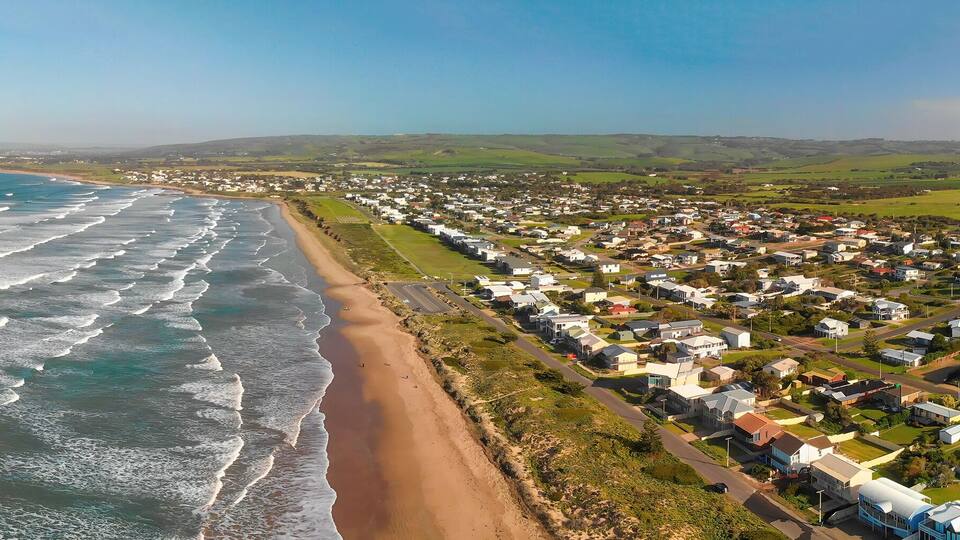 A coastal town with a beach, houses, and rolling hills in the background.