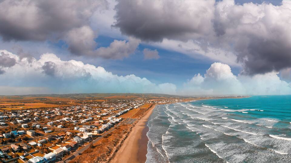 A coastal town with a beach, ocean waves, and a cloudy sky.