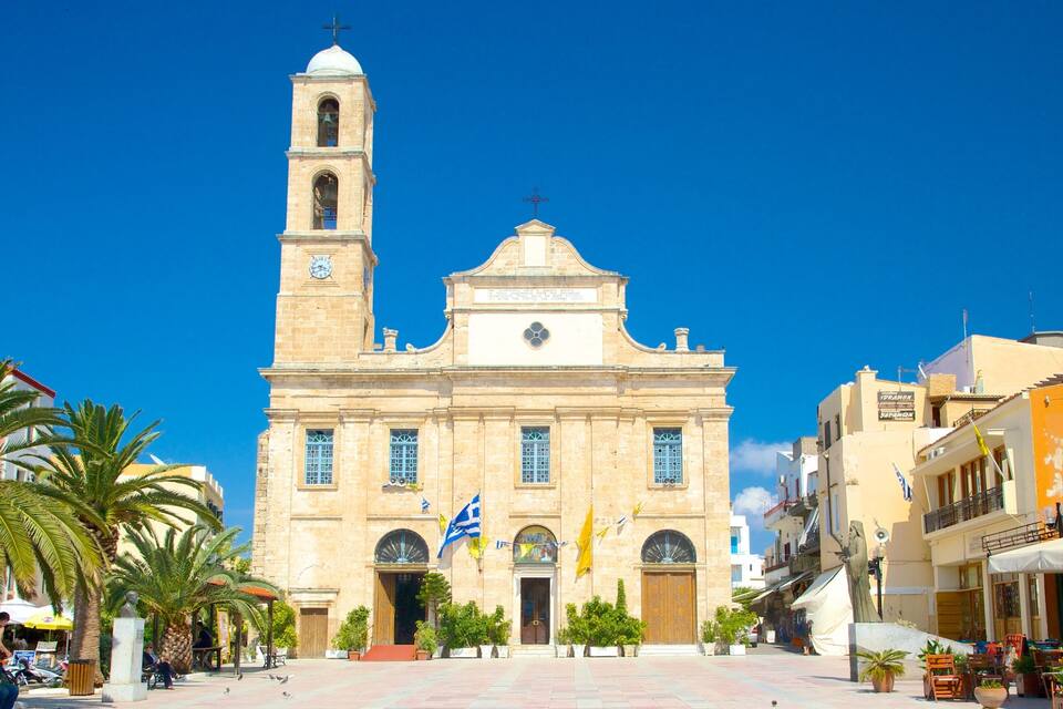 Una iglesia histórica con un campanario y una cúpula, rodeada de palmeras y un cielo azul despejado.