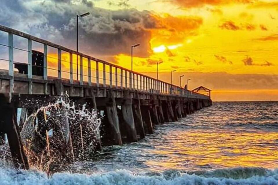 Une jetée qui s’avance dans l’océan, avec des vagues qui s’y brisent sous un ciel au coucher du soleil.