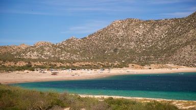A coastal landscape with a beach, clear turquoise waters, and a mountainous backdrop.