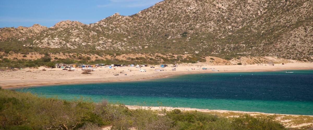 A coastal landscape with a beach, clear turquoise waters, and a mountainous backdrop.