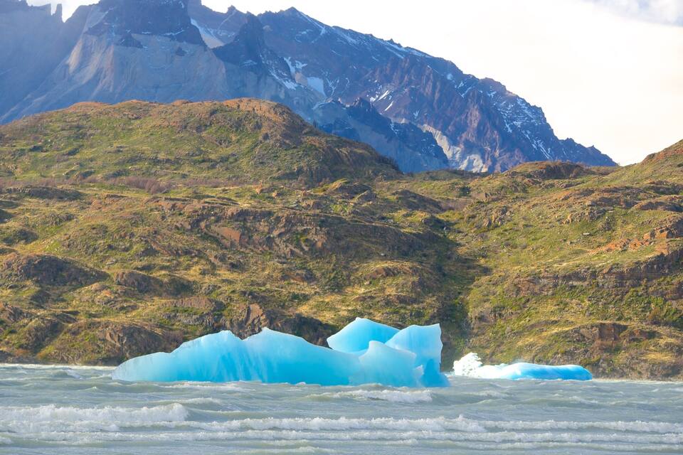 A glacier with icebergs in a fjord, surrounded by rugged mountains.