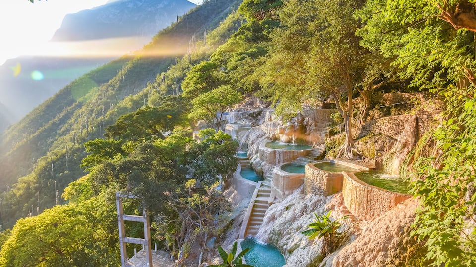 Terraced pools on a hillside, surrounded by lush greenery and mountains.