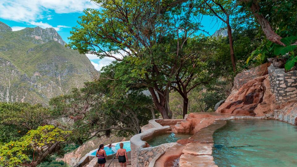 A natural hot spring surrounded by lush greenery and rocky terrain.