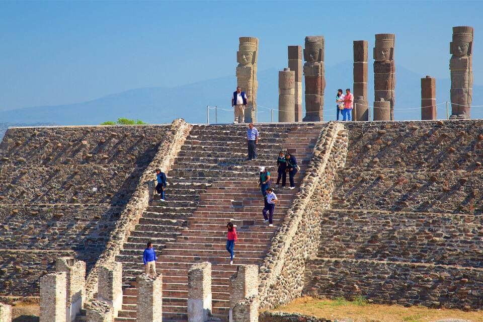 Una escalera de piedra conduce a una plataforma con grandes columnas de piedra y un cielo despejado al fondo.