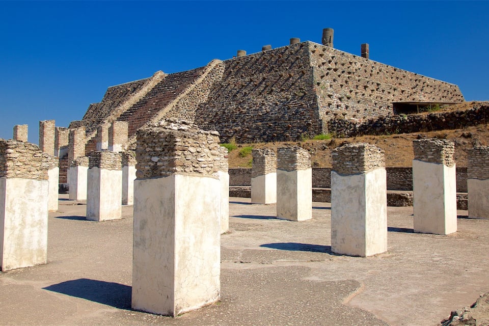 Ancient ruins with stone columns and a pyramid-like structure.