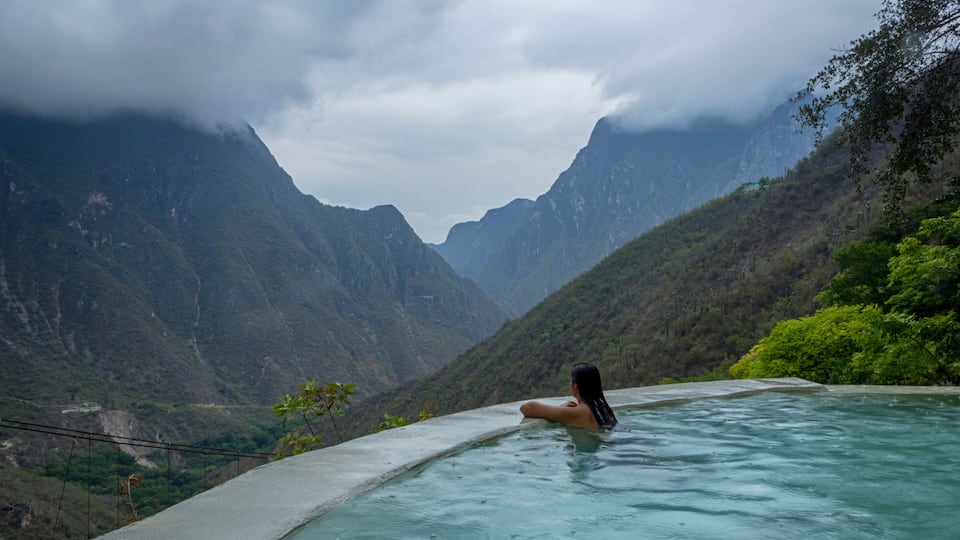 A person in a infinity pool overlooking a mountainous landscape.