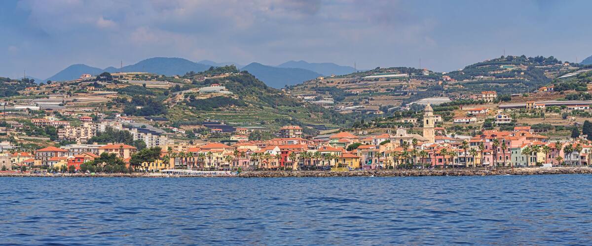 A coastal town with colorful buildings, a prominent church, and hills in the background.