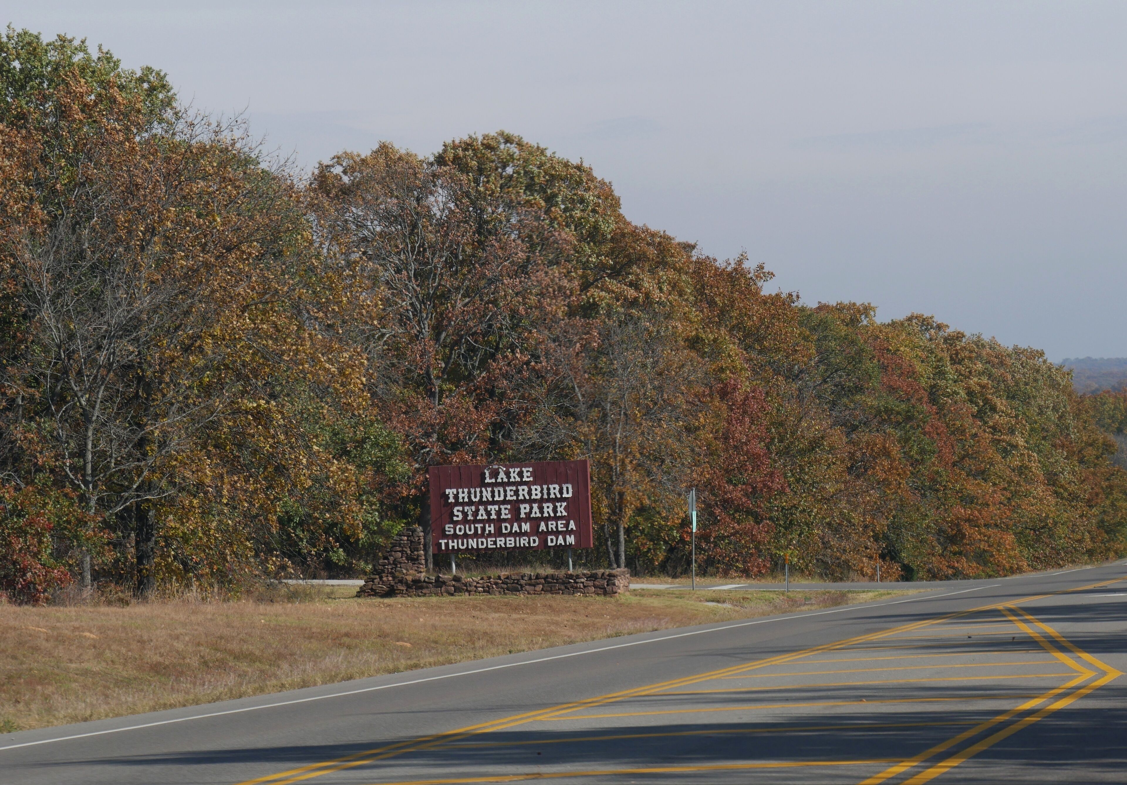 Huge billboard sign by the roadside along the Lake Thunderbird State Park in Oklahoma with fall colors in the trees in November 2017.