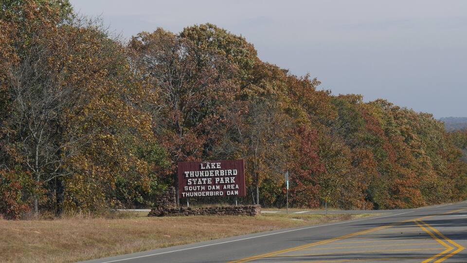 A road with a sign for Lake Thunderbird State Park South Dam Area.