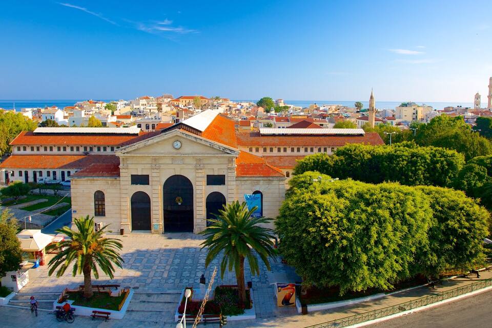 A historic building with a clock tower, surrounded by lush greenery and a coastal cityscape in the background.