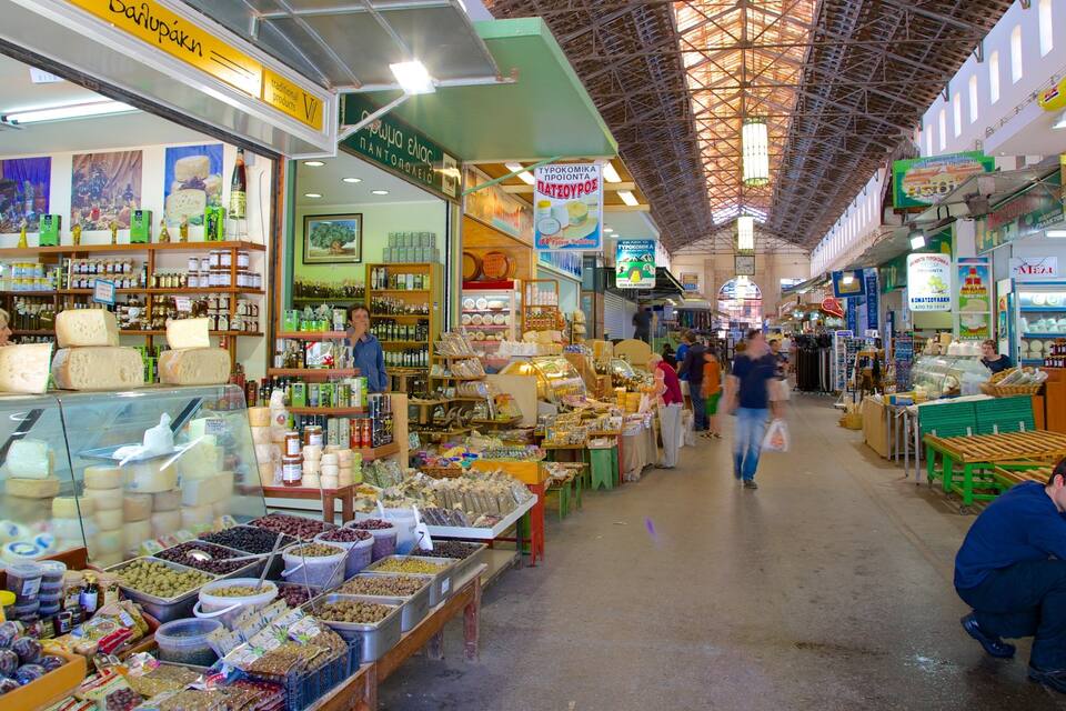 Ein belebter Innenmarkt mit verschiedenen Ständen, die Käse, Oliven und andere Lebensmittel anbieten.