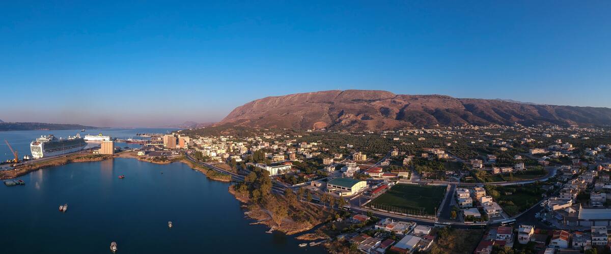 A coastal city with a large cruise ship docked, a mountain in the background, and a mix of residential and commercial buildings.