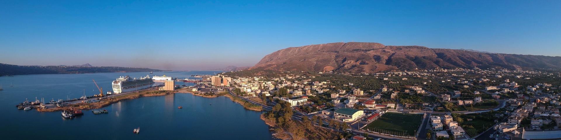 A coastal city with a large cruise ship docked, a mountain in the background, and a mix of residential and commercial buildings.