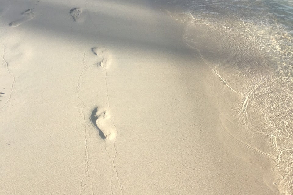 Una playa arenosa con huellas que se adentran en el agua.