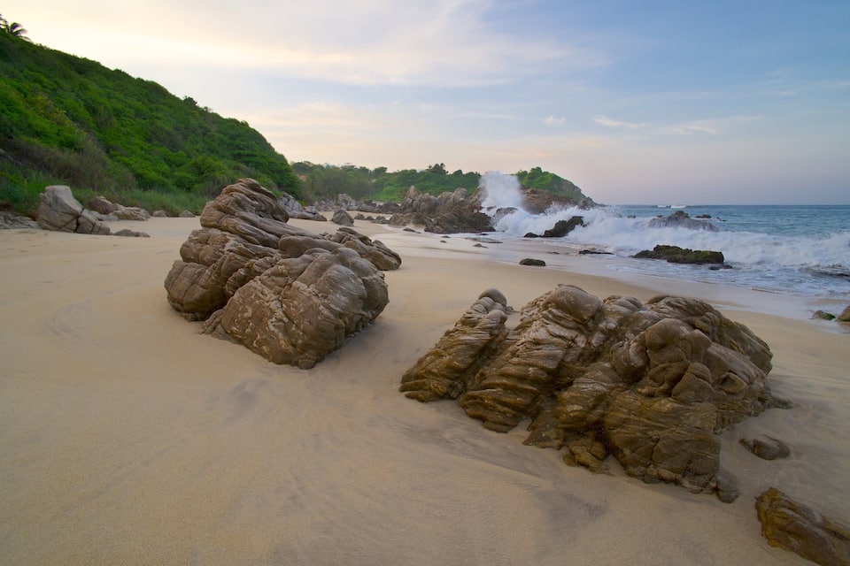 Une plage de sable avec de grandes formations rocheuses et des vagues qui déferlent sur le rivage.