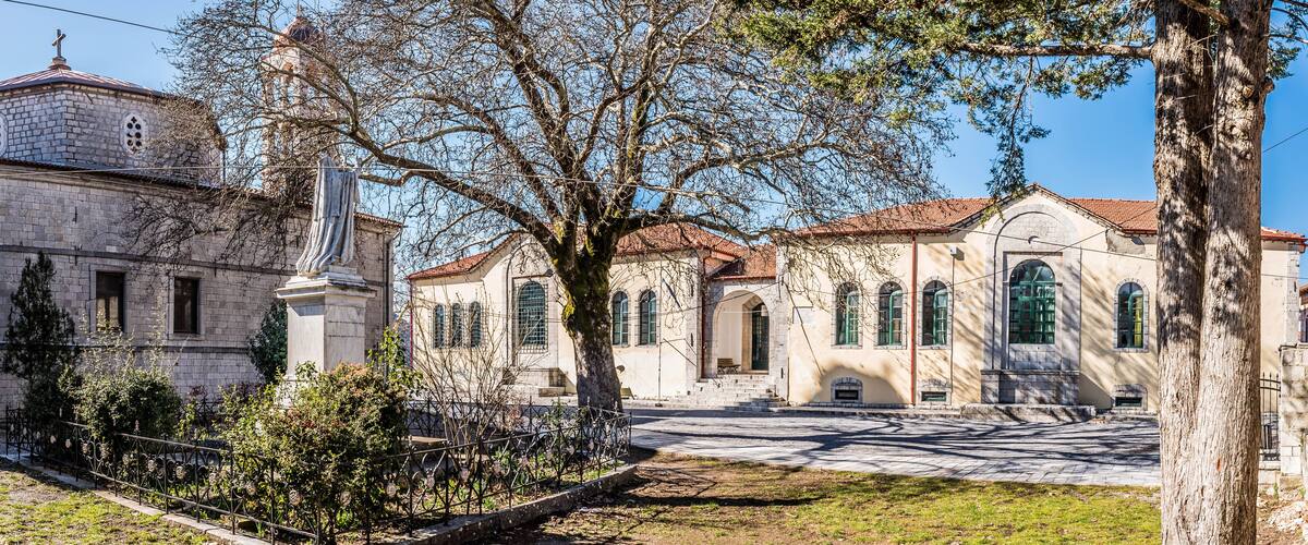 A historic building with a dome and arched windows, surrounded by trees and a paved courtyard.