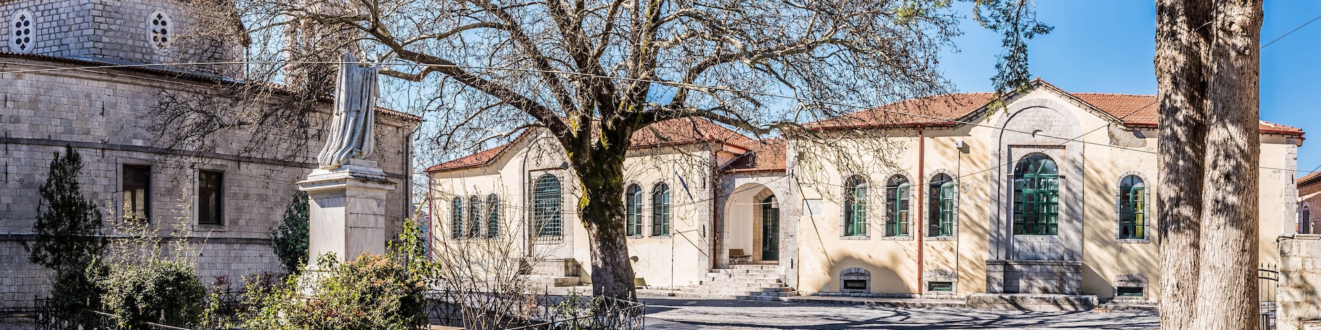 A historic building with a dome and arched windows, surrounded by trees and a paved courtyard.