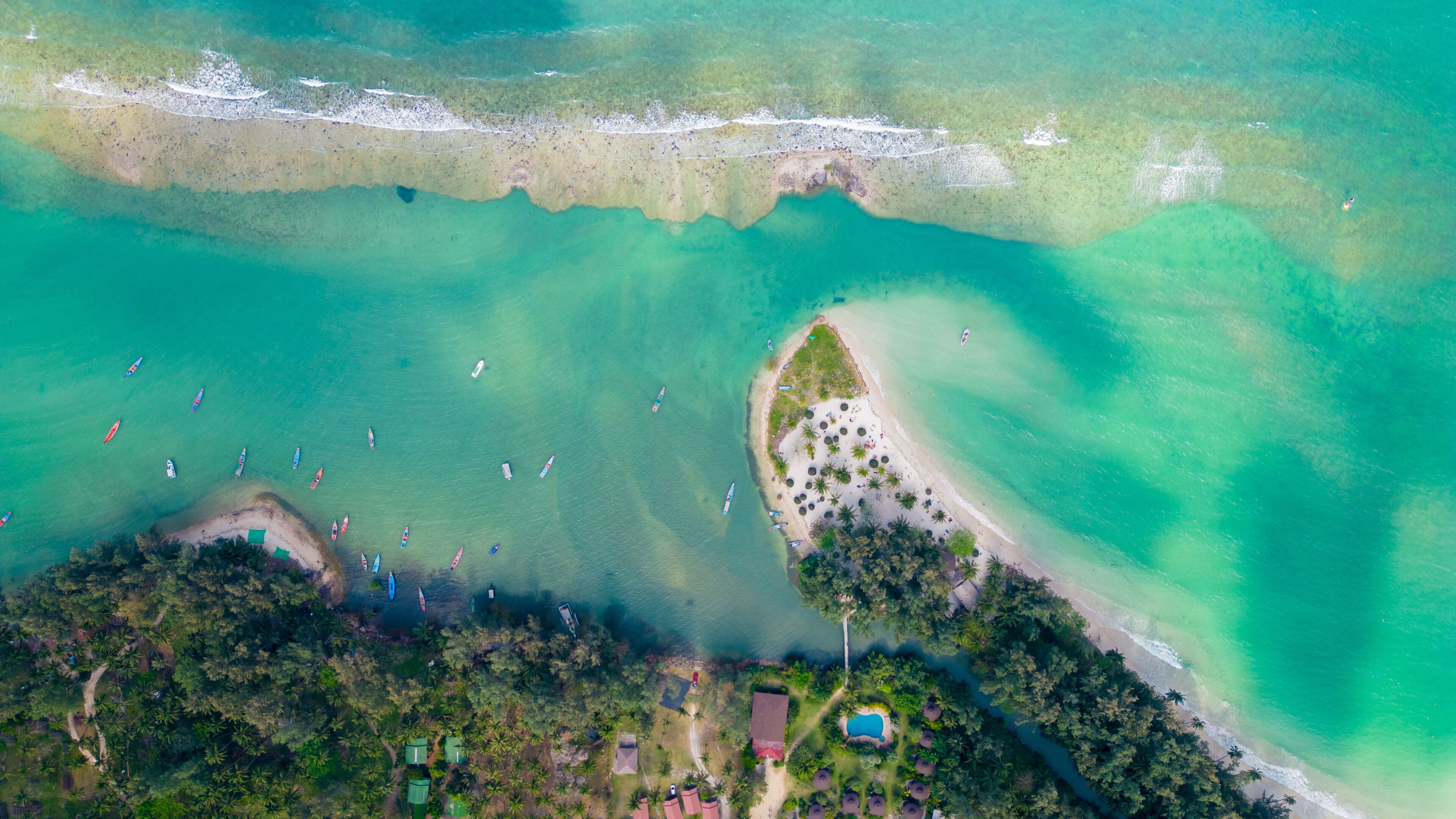 An aerial view of a tropical beach with clear turquoise waters, a sandy beach, and several boats.