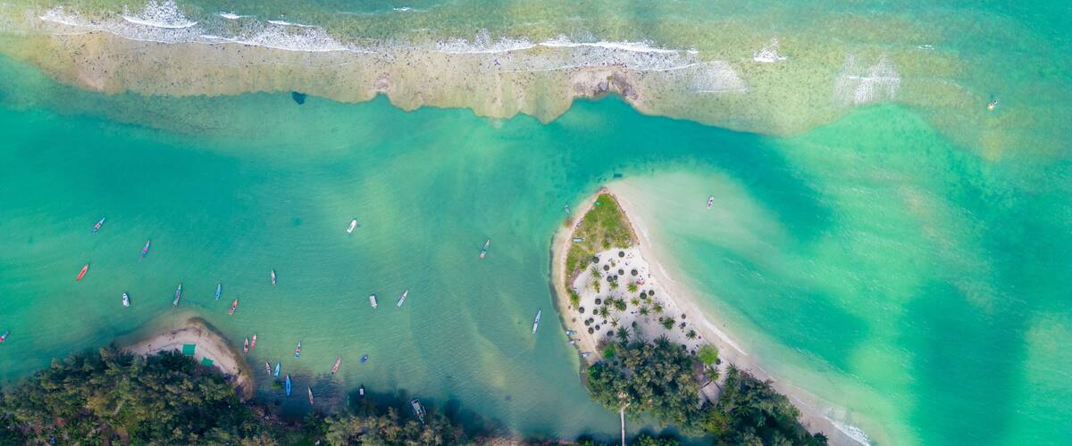 An aerial view of a tropical beach with clear turquoise waters, a sandy beach, and several boats.