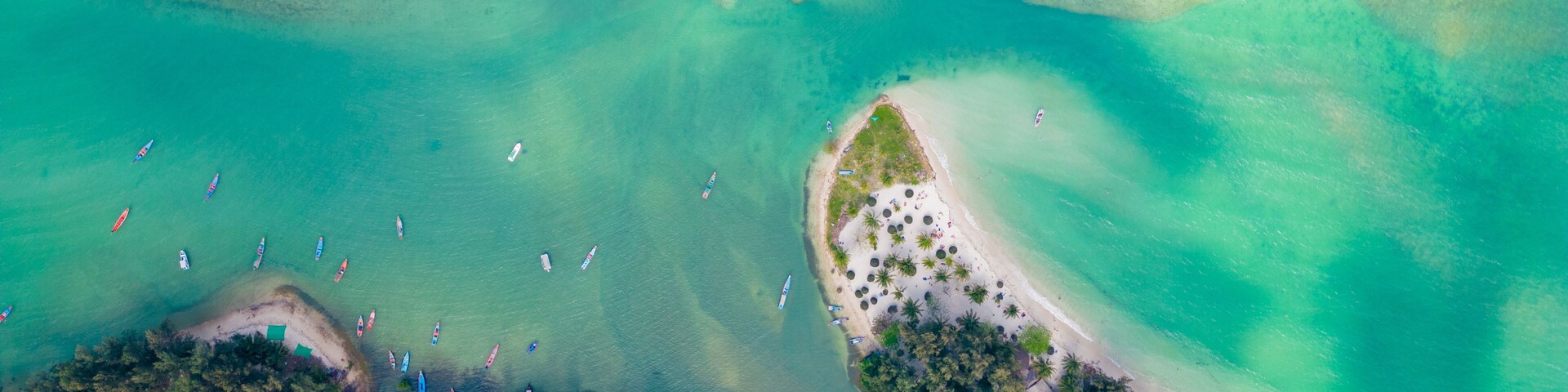 An aerial view of a tropical beach with clear turquoise waters, a sandy beach, and several boats.