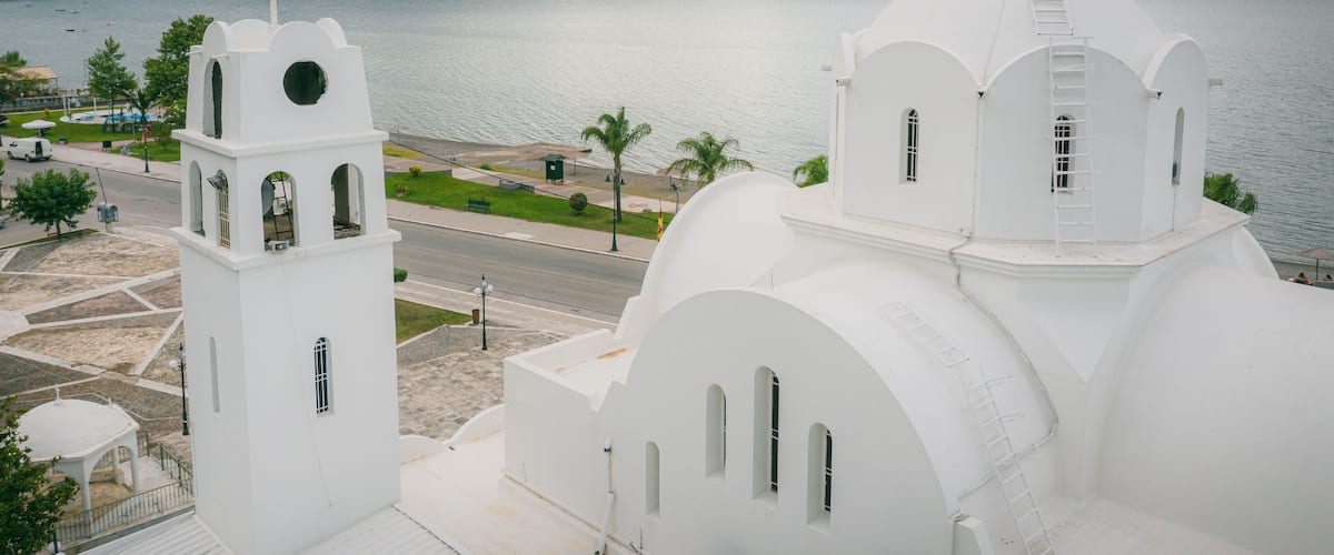 A white church with two towers and a dome, overlooking a calm lake with mountains in the background.