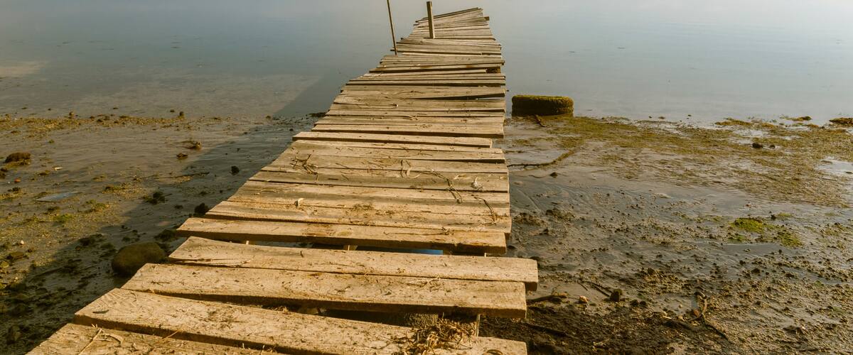 A wooden pier extending into calm water with distant mountains.