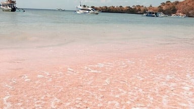 Praia arenosa rosa com um objeto em forma de coração em primeiro plano e barcos ao fundo.
