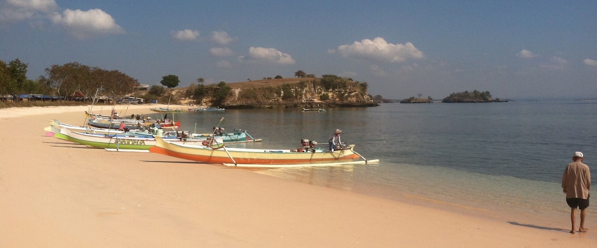 A beach with boats and a person standing on the shore.