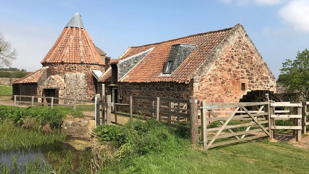 Ein Steinhaus mit einem kegelförmigen Dach und einem Wasserrad.