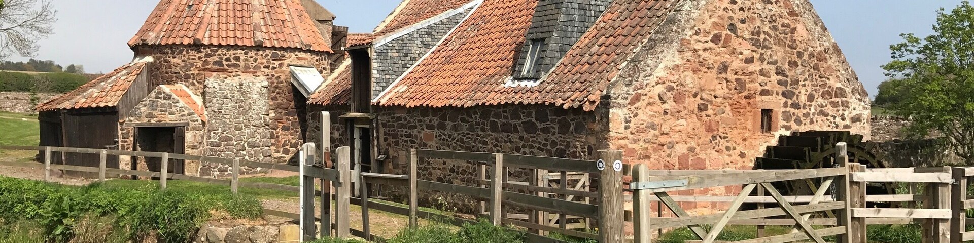 Um edifício de pedra com telhado cônico e uma roda d'água.