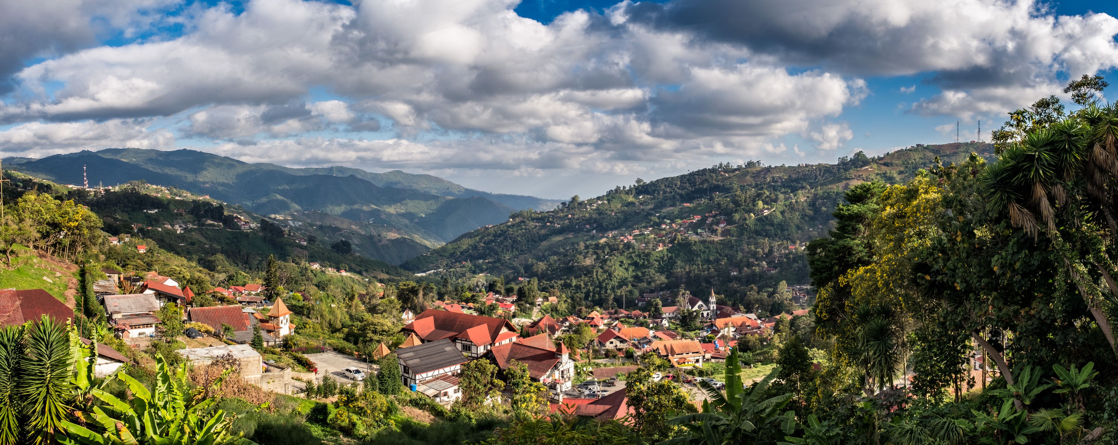 Un paysage montagneux avec un village, des maisons aux toits rouges et une végétation luxuriante.