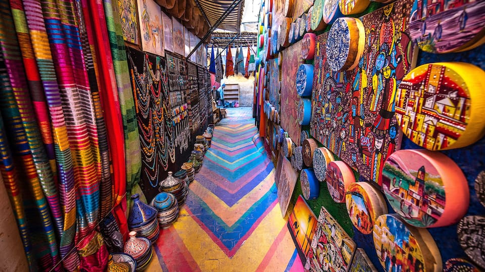 A vibrant market with colorful textiles, ceramics, and paintings.