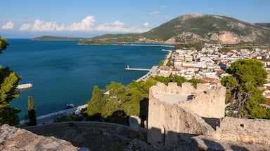 A coastal town with a historic stone wall, a clear blue sea, and a mountain in the background.