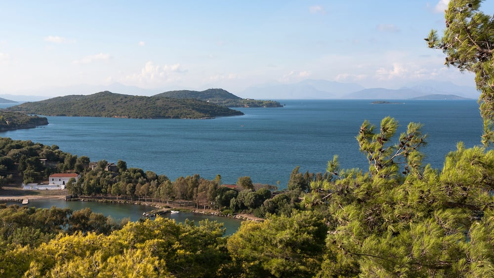 Eine Küstenlandschaft mit freiem Blick auf das Meer, einer kleinen Insel und einem gebirgigen Hintergrund.