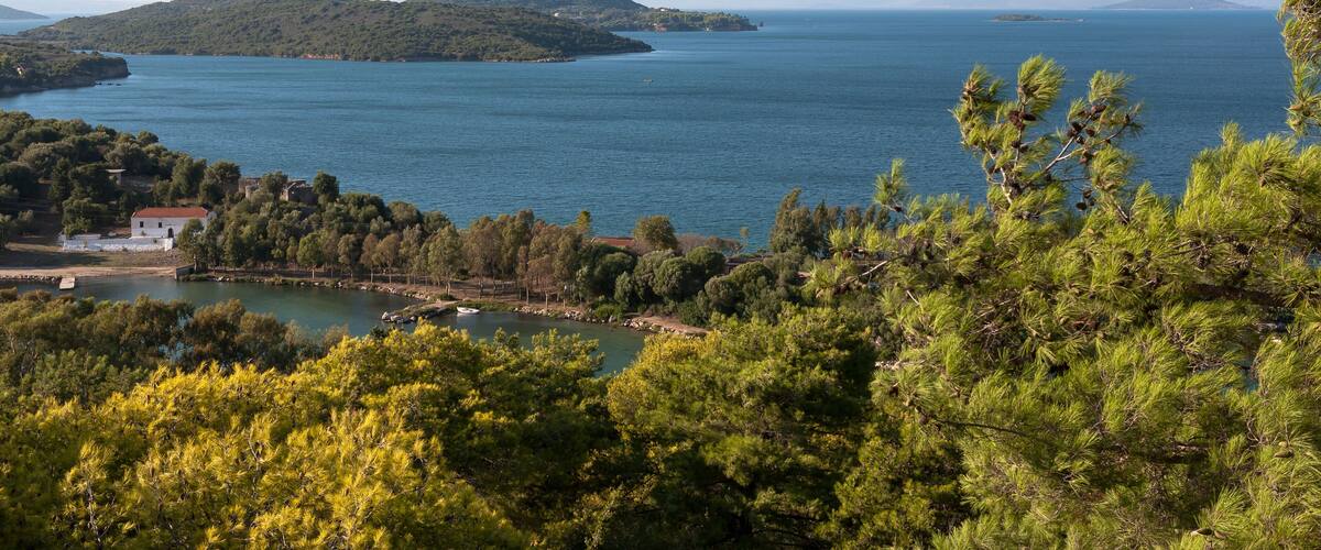A coastal landscape with a clear view of the sea, a small island, and a mountainous background.