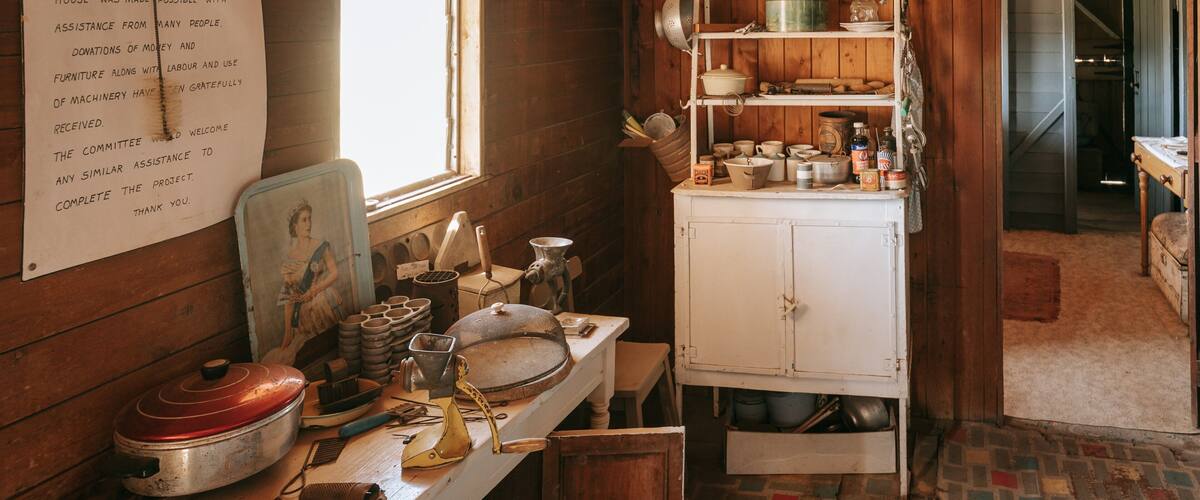 A rustic kitchen with wooden walls, a white cabinet, and vintage kitchenware.