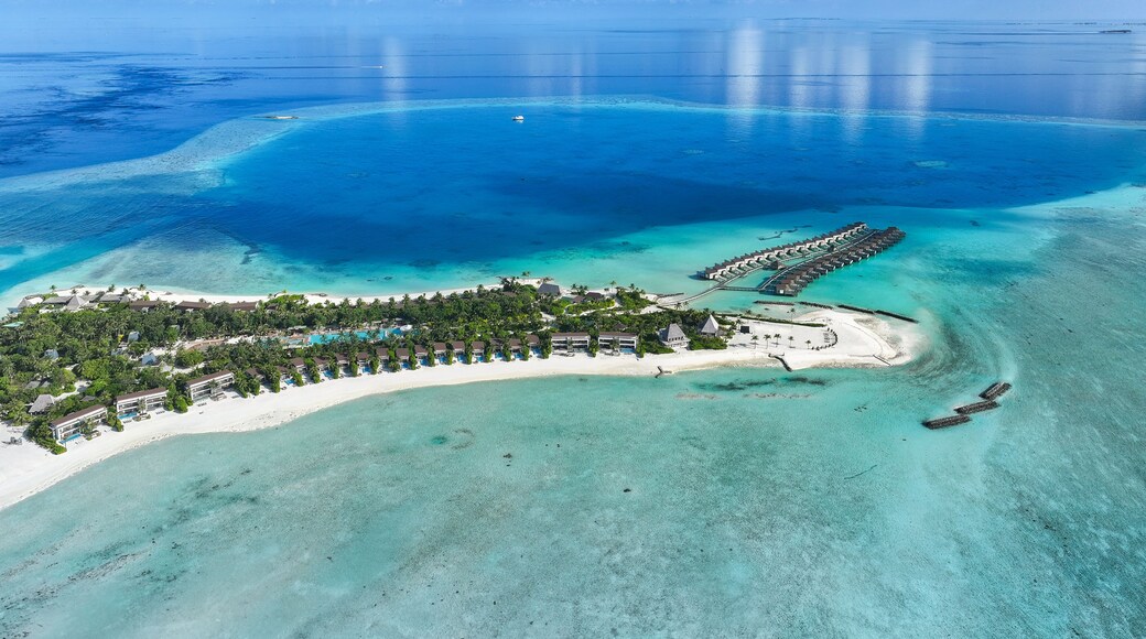 Aerial view of turquoise waters embracing the sandy shores of a tropical island resort with overwater bungalows, Thulusdhoo, Kaafu Atoll, Maldives.