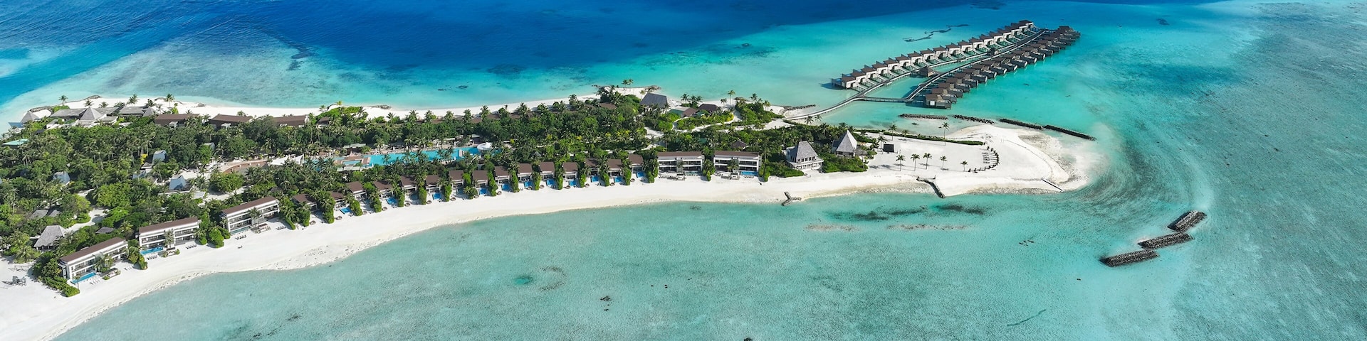 Aerial view of turquoise waters embracing the sandy shores of a tropical island resort with overwater bungalows, Thulusdhoo, Kaafu Atoll, Maldives.
